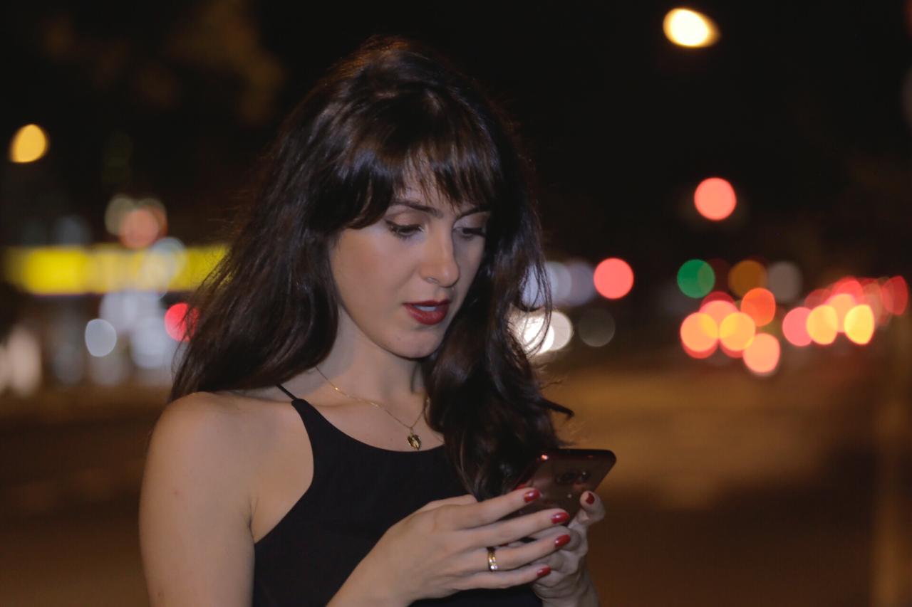 Mulher olhando tela de celular à noite no meio da rua