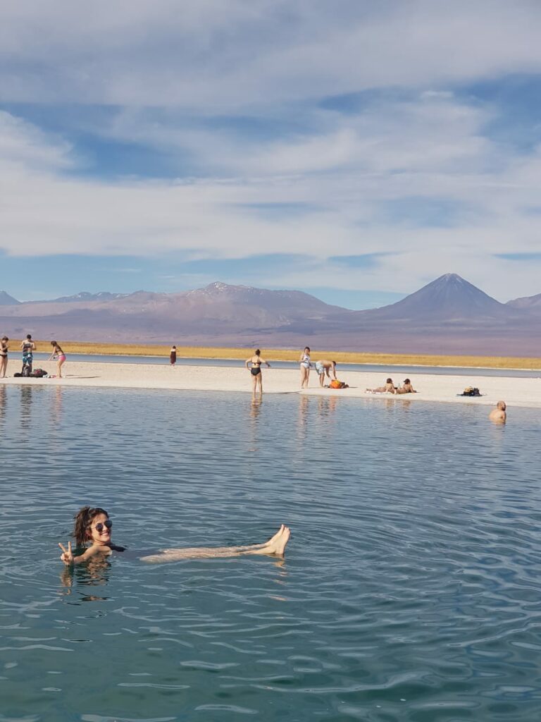 Moça feliz flutuando na Laguna Cejar com vulcão ao fundo