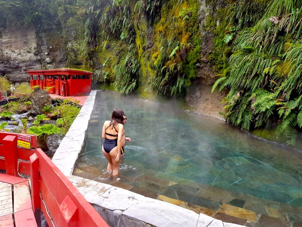 Casal entrando em piscina natural de água quente com natureza ao redor