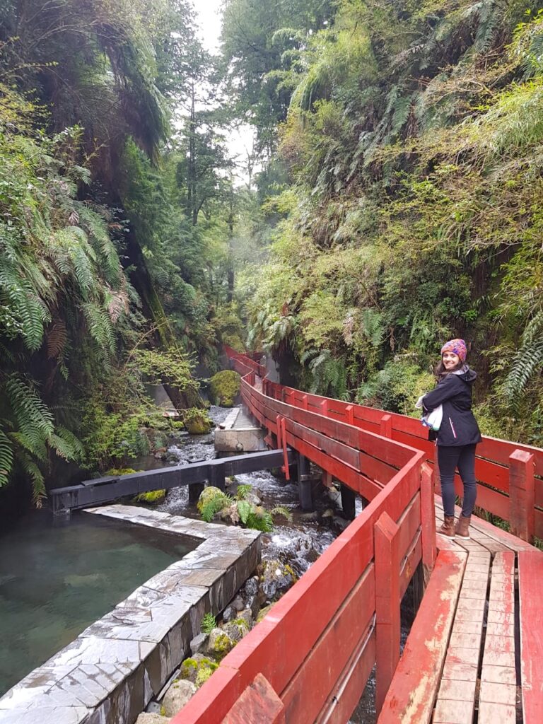 Mulher parada m longa passarela de madeira vermelha no meio da floresta e sob rio de água quente natural
