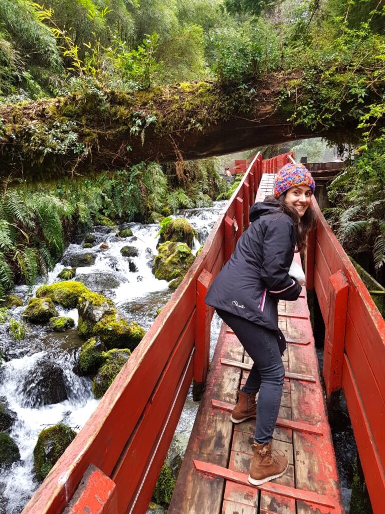 Mulher passando em passarela de madeira vermelha com rio embaixo 