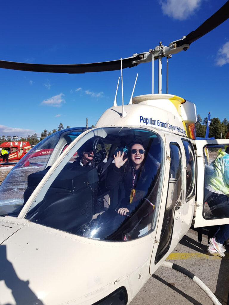 Moça sorrindo dentro de helicóptero junto com pilota depois de sobrevoar o Grand Canyon